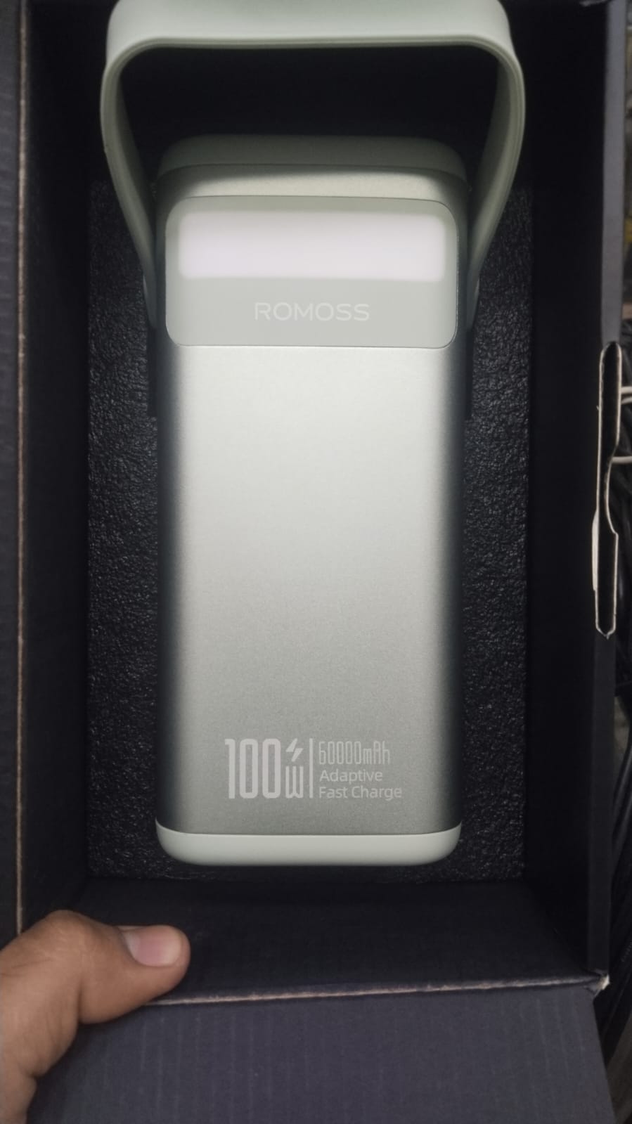 Silver Romoss 100W 60000mAh power bank unboxed and resting inside its black protective packaging tray showing the built-in handle and front LED light bar.
