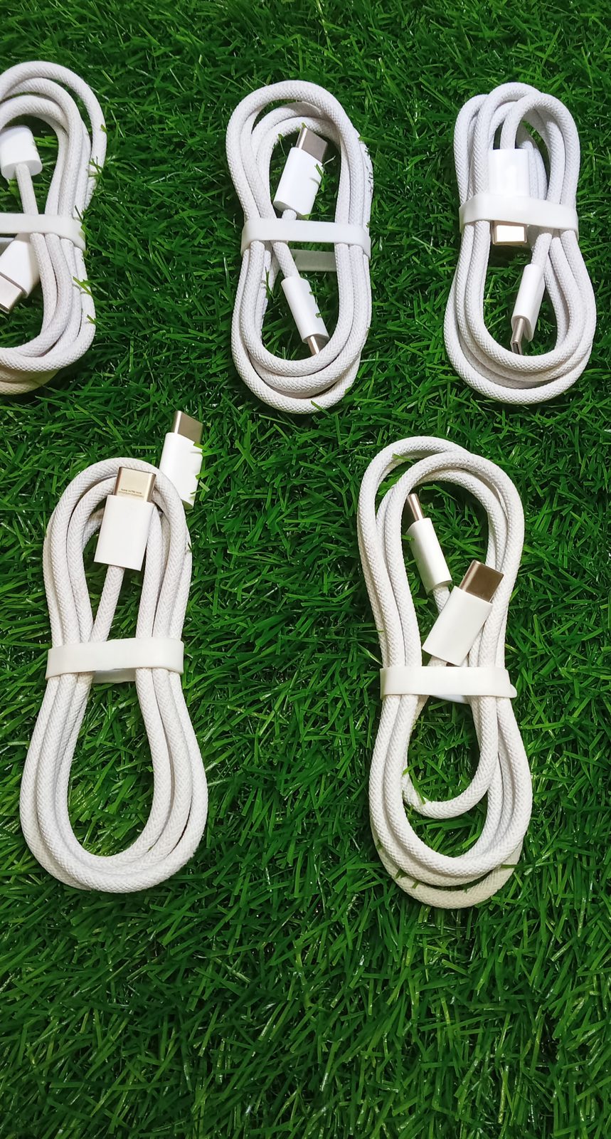 Close-up view showing six neatly coiled Original Apple Braided Type-C Cables arranged on green grass background by M F Chargers.