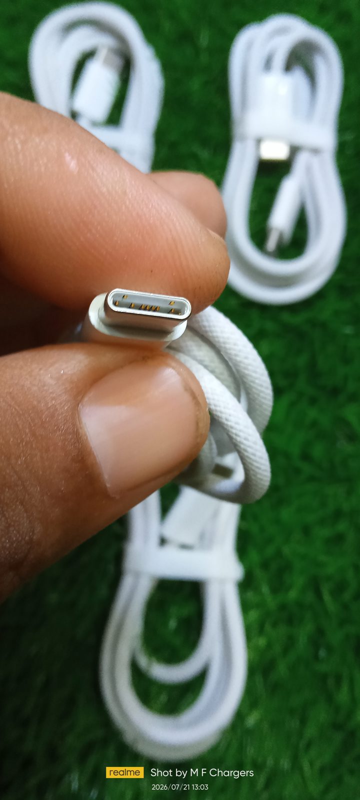 Fingers showing the metal Type-C connector tip and gold pins of an Original Apple Braided Type-C to Type-C Cable up close at M F Chargers.
