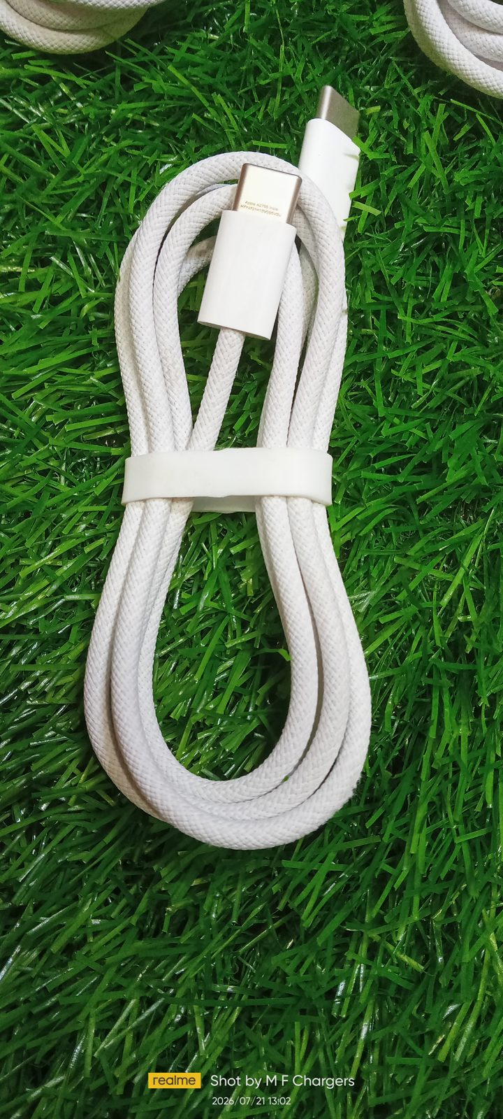 Detailed view of a coiled white Original Apple Braided Type-C to Type-C Cable with paper band, on a green background at M F Chargers.